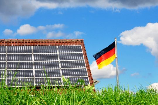 Hausdach voller Solarpaneele, daneben weht eine Deutschlandfahne.