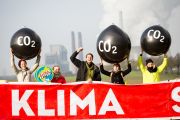Ein paar Leute halten sehr große schwarze Ballons mit der Aufschrift CO₂ hoch, vorn ein Transparent mit der Aufschrift: Klima, im Hintergrund ein Kohlekraftwerk.