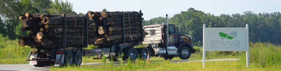 Mit Rundholz beladener Truck fährt an einem Enviva-Firmenschild vorbei.