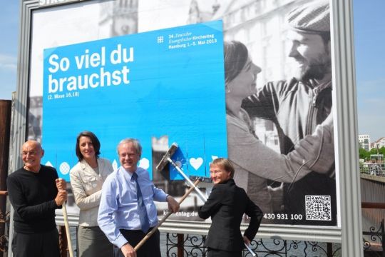 Persönlichkeiten der evangelischen Kirche bringen öffentlichkeitswirksam ein Großplakat an mit der Aufschrift: 