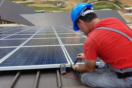 Ein Monteur befestigt Solarmodule auf einem Dach.