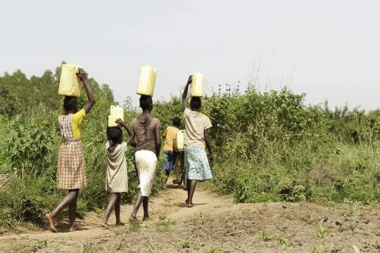 Mädchen laufen mit Wasserkanistern auf dem Kopf
