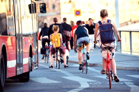 Einige jüngere Menschen fahren auf einer Straße neben einem Bus.