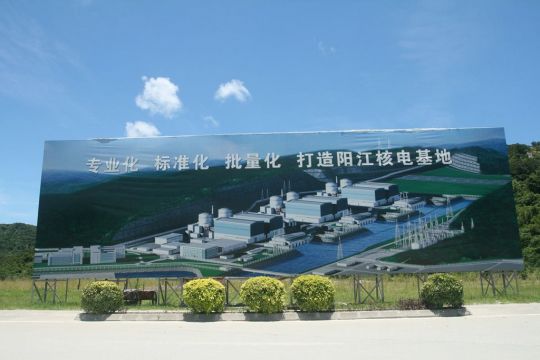 Riesige Bautafel vor Wald und Wiese, darauf steht auf Chinesisch: Bau des Kernkraftwerks Yangjiang.