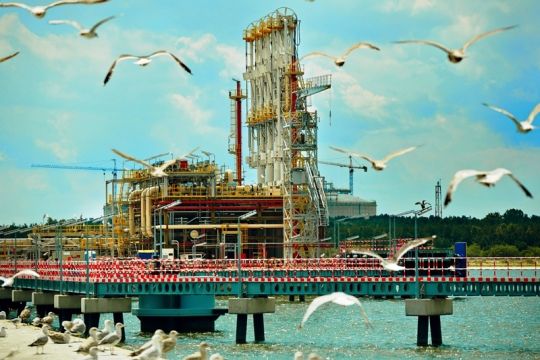 In den Himmel aufragende Anlagen des Flüssigerdgas-Terminals Swinemünde an der Ostsee, im Vordergrund fliegen Möwen.