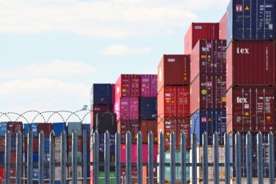 Aufgestapelte Container, davor ein stacheldrahtbewehrter Zaun.