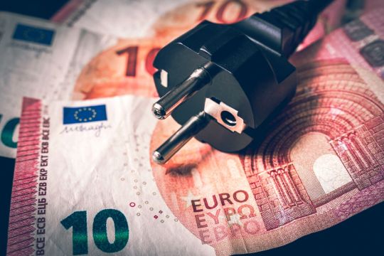 Schwarzer Strom-Stecker, darunter rotbraune Zehn-Euro-Scheine, etwas geheimnisvoll ausgeleuchtet.