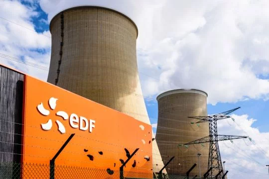 Logo des Betreibers EDF am Eingang des Atomkraftwerks Nogent-sur-Seine, im Hintergrund die beiden Kühltürme.