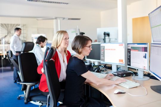 Zwei Frauen betrachten die Kurse von CO2-Zertifikaten auf einem Monitor.