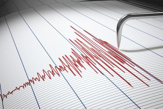 Ein Seismograf zeichnet eine rote Kurve auf Papier, die gerade mächtig ausschlägt.