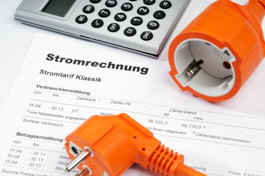Stromrechnung mit Stecker und Buchse in Orange und einem Taschenrechner.