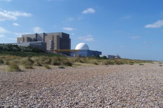 Steinige Nordseeküste im County Suffolk, gleich hinter den Dünen stehen ein klobiges dunkelgraues und ein modernes weiß-blaues Atomkraftwerk.