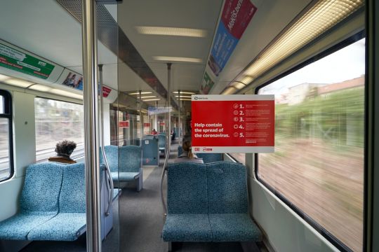 Spärlich besetzte Regionalbahn mit einem Schild in englischer Sprache: Helfen Sie, die Verbreitung des Coronavirus zu begrenzen.