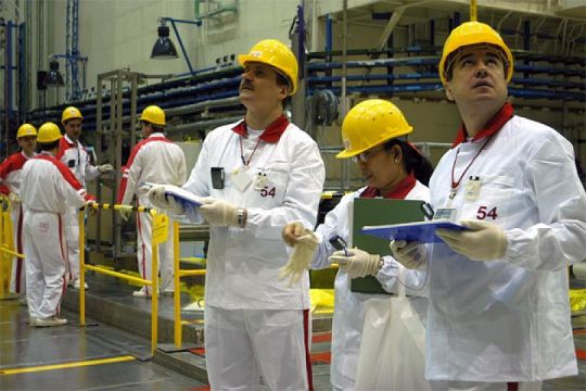 Weiß gekleidete Personen mit gelben Helmen stehen in der Kraftwerkshalle, schauen in verschiedene Richtungen und notieren sich etwas.