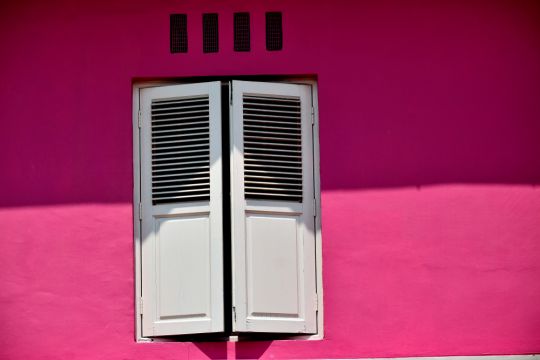 Fast geschlossene Fensterläden in einem pinkfarbenen Ladenwohnhaus im historischen Viertel Kampong Glam in Singapur.