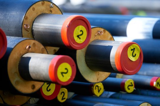Neue Fernwärme-Rohrleitungen mit den typischen roten Schutzabdeckungen liegen auf einem Stapel, alle sind mit einem runden gelben Aufkleber gekennzeichnet, auf dem die Zahl 2 steht.