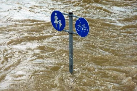 Verkehrsschild, dass einen Geh- und Radweg anzeigt, steht im heftig fließenden Wasser.