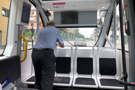 Ein Mitarbeiter der Wiener Linien steht gebückt in einem leeren Shuttlebus und schaut durch das relativ kleine Frontfenster, die Hände an der Steuerbox.