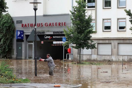 Ein Mann steht auf der überfluteten Rathausstraße in Hagen knietief im Wasser und streckt die Arme aus.