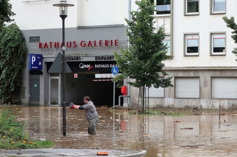 Ein Mann steht auf der überfluteten Rathausstraße in Hagen knietief im Wasser und streckt die Arme aus.