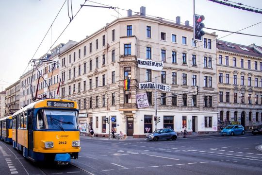 Straßenbahn fährt an besetztem Haus in Leipzig vorbei, daran ein Transparent: Grenzenlose Solidarität.