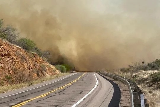 Eine leere Landstraße führt in eine rauchverhangene Feuerzone, die Weiterfahrt ist offensichtlich gefährlich oder unmöglich.