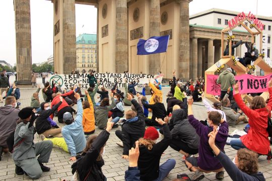 Menschen sitzen vor dem Brandenburger Tor.