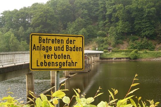 Brücke über die Wupper mit Stauwehr, im Vordergrund ein gelbes Schild: Betreten der Anlage und Baden verboten – Lebensgefahr.