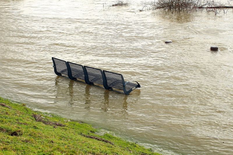 Eine Bank steht am Flussufer bis knapp unter die Sitzfläche im Wasser.