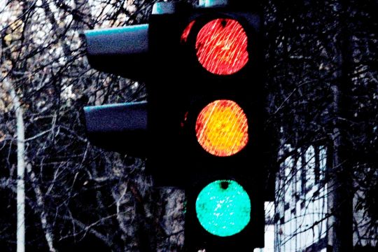 Eine Ampel vor dunklem Hintergrund leuchtet gleichzeitig in rot, gelb und grün.