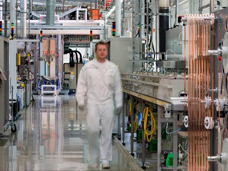 Vor 2012: Weiß gekleideter Solararbeiter geht durch die Fertigungshalle einer Solarfabrik der damaligen Firma Odersun im Land Brandenburg.