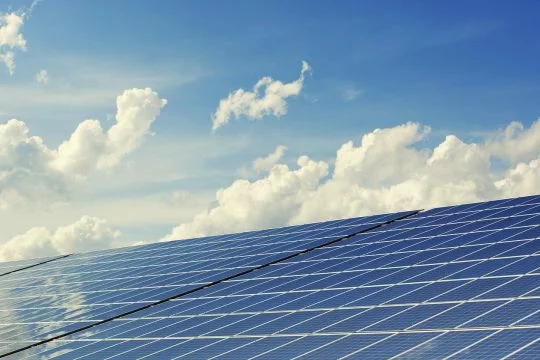 Große schräge Photovoltaikfläche vor hellblauem Himmel mit weißen Wolken.