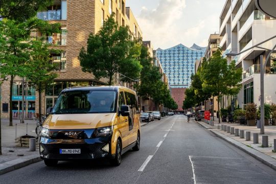 Senfgelber Kleinbus des Ridepooling-Unternehmens Moia in einer Hamburger Straße, im Hintergrund die Elbphilharmonie.