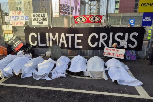 Eine Gruppe Protestierender liegt wie tot auf dem Boden, mit weißen Tüchern bedeckt, dahinter ein Transparent: Klimakrise.