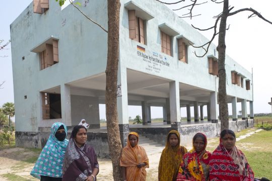 Einige bangladeschische Frauen stehen vor einem weißen Zyklon-Hochbunker.