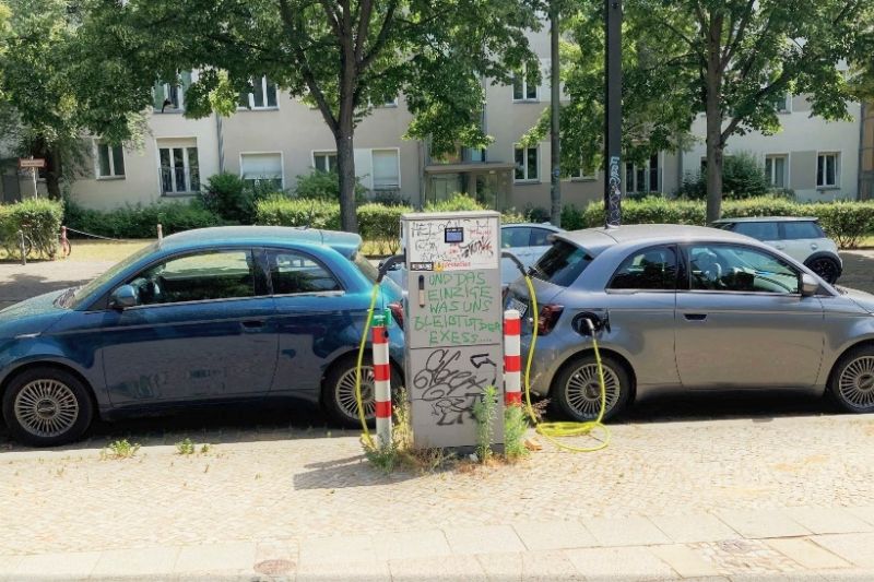 Zwei elektrische Kleinwagen werden an einer Ladesäule in einem Wohngebiet aufgeladen.