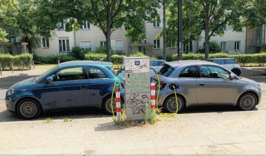 Zwei elektrische Kleinwagen werden an einer Ladesäule in einem Wohngebiet aufgeladen.