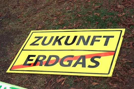 Auf dem Boden liegt ein gelbes Schild, das wie ein Ortsschild aussieht. Oben steht: Zukunft. Unten steht durchgestrichen: Erdgas.