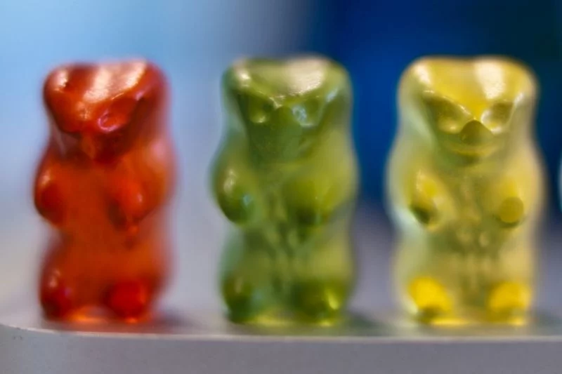Ein rotes, ein grünes und ein gelbes Gummibärchen stehen nebeneinander, etwas verschwommen fotografiert.