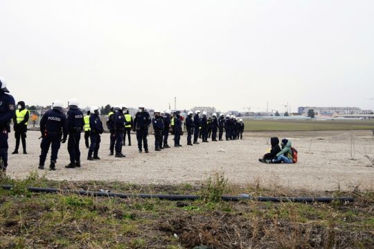 Zwei Menschen sitzen auf der Schnellstraßen-Trasse, vor ihnen eine Polizeikette.