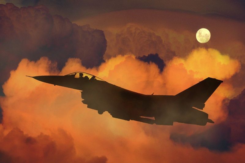 Silhouette des US-Militärjets F-16 vor orangefarbenem Himmel, im Hintergrund der Mond.
