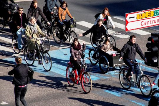 Ein Dutzend Radfahrerinnen und Radfahrer auf einem breiten Fahrradstreifen, einige geben Handzeichen.