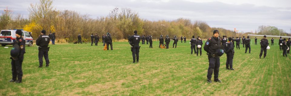 Einige Dutzend Einsatzkräfte der Polizei stehen verteilt auf einer großen Wiese herum.