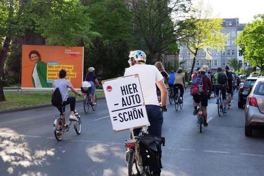 Ein Teilnehmer einer Fahrraddemo hat am Rad ein Schild befestigt, auf dem steht im Schema einer Subtraktionsrechnung: Hier minus Auto gleich schön.