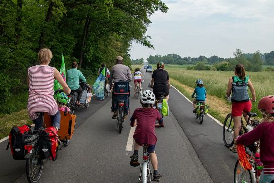 Fahrraddemo gegen Autobahnausbau in Niedersachsen, einige Erwachsene und Kinder fahren eine Landstraße zwischen Wald und Feld entlang, voran ein Polizeiauto.