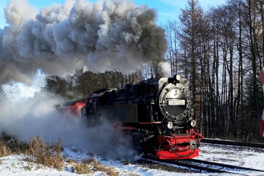 Eine kleine Dampflok fährt aus Schornstein und Blasrohr dampfend durch den Winterwald.