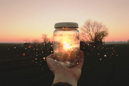 Eine Hand hält ein Glas mit Schraubdeckel vor die untergehende Sonne, sodass die Sonne scheinbar im Glas gefangen ist.