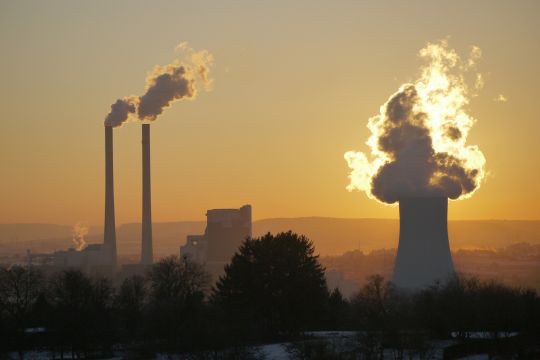 Kraftwerk Heilbronn mit zwei rauchenden Schornsteinen und dampfendem Kühlturm vor einem Sonnenuntergang.