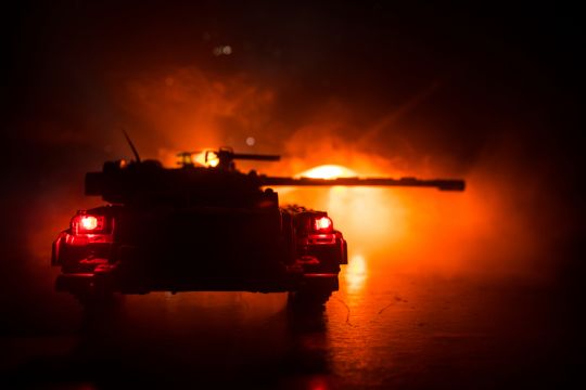 Ein Panzer mit zur Seite gerichtetem Rohr vor nächtlichem Feuerschein.