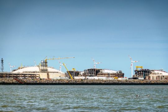 Drei große, flache, hellgraue Kuppeln mit einigen Rohrleitungen hinter einer Kaimauer an der Nordsee.